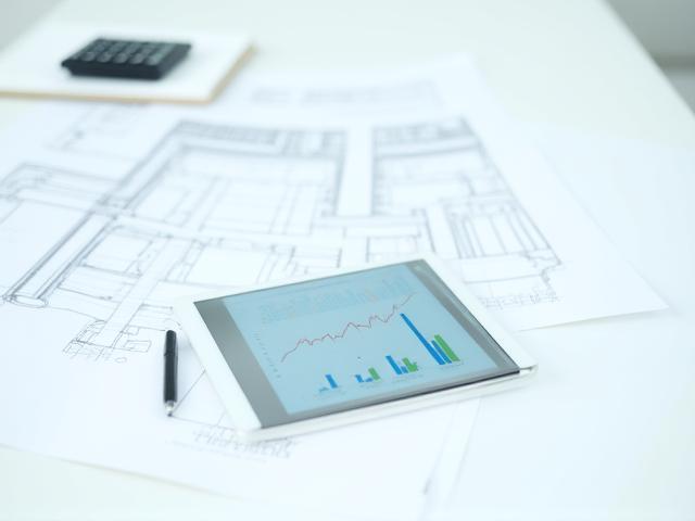 Architectural plans and a tablet on a desk, symbolizing strategic roof maintenance planning.
